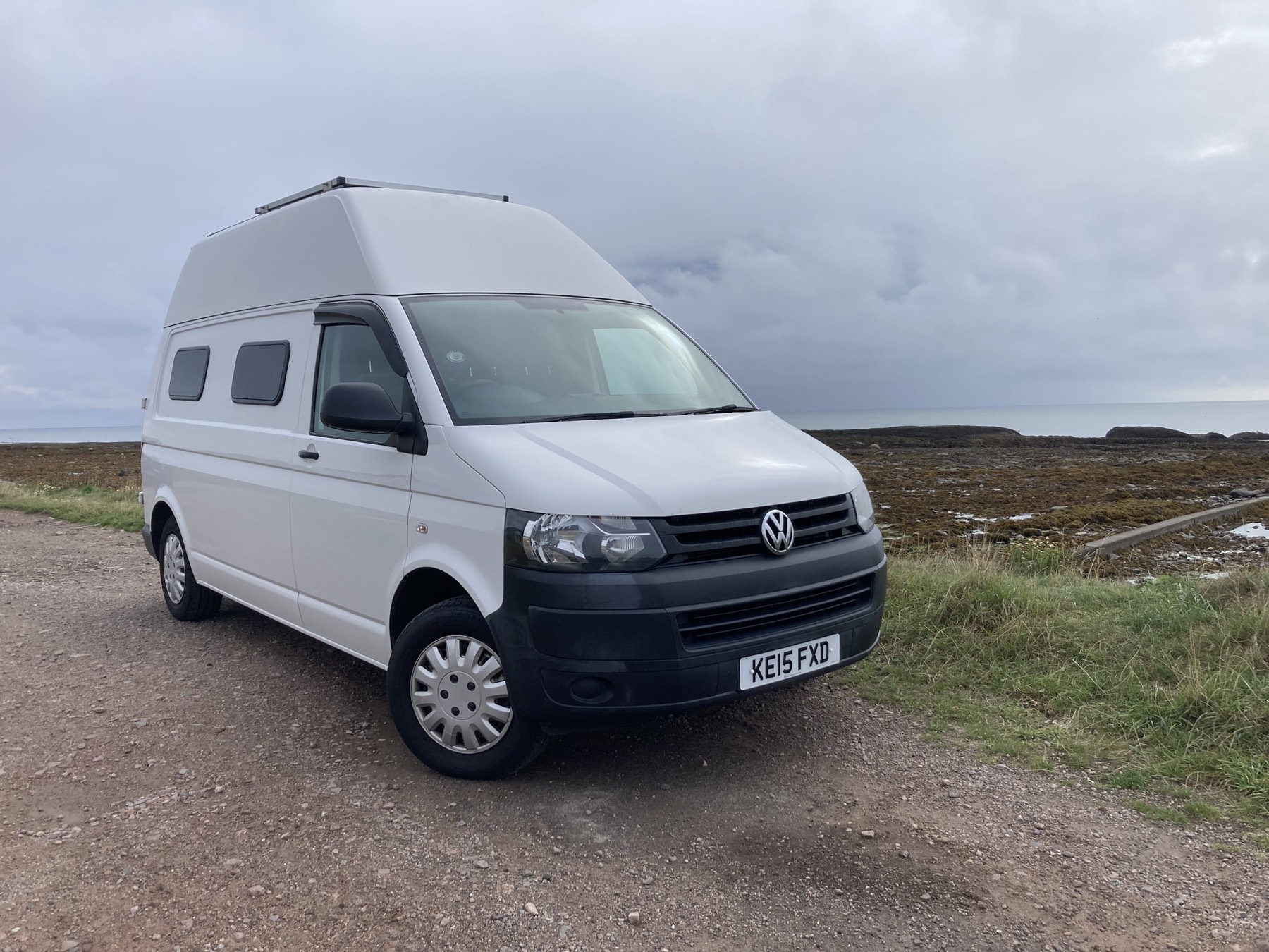 Lola, a white 2015 Volkswagen Transporter T30 high-top, parked on a coastal gravel track